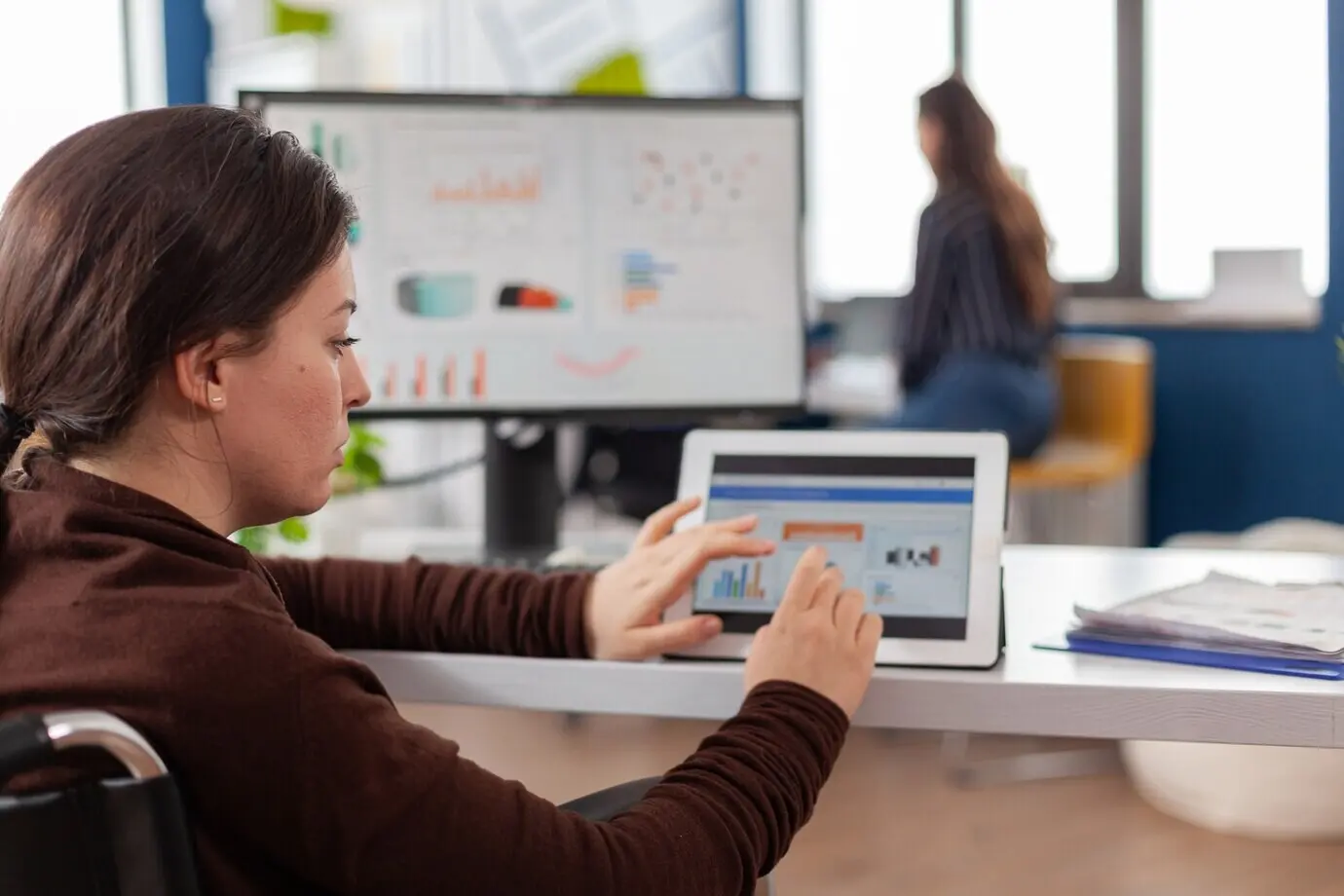 Женщина-предприниматель использует компьютер и планшет, проверяя статистические данные в офисе стартапа.